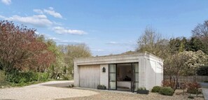Ein modernes, eingeschossiges Gebäude mit Garage, einem Schlafzimmer mit Bett und Schreibtisch sowie einer kleinen Außenfläche.