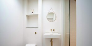 Ein Badezimmer mit einem weißen Waschbecken, einem runden Spiegel und einem kleinen Regal mit einem Schilferdiffusor.