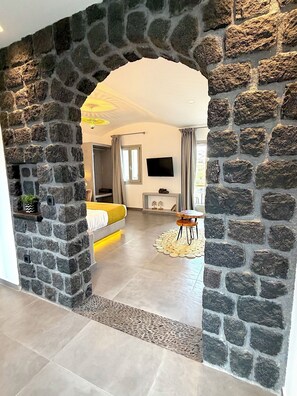A modern room with a stone archway, a bed, a TV, and a small table. - Villa Samaros (Karterádos)