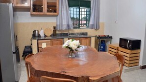 A kitchen with a round wooden table, wooden chairs, a refrigerator, a microwave, and a window with curtains. - Beautiful 2-bedroom corporate apartments within  Entebbe (Entebbe)