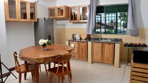 A kitchen with wooden cabinets, a dining table with chairs, a refrigerator, and a window with curtains. - Beautiful 2-bedroom corporate apartments within  Entebbe (Entebbe)