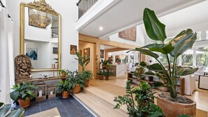Um interior amplo com um espelho grande, plantas em vasos e uma escadaria que leva a um andar superior.