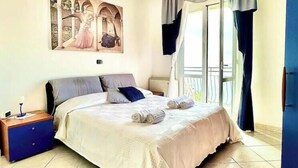 Une chambre à coucher avec un lit, une table de chevet, un tableau, une fenêtre avec des rideaux et un balcon.