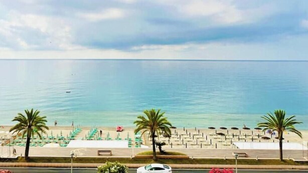 Une plage avec des palmiers, une promenade et une mer calme.