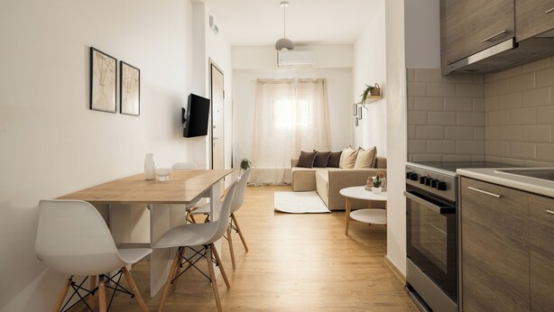 Une cuisine moderne dotée d’un four encastré, un coin repas avec une table et des chaises en bois, et un espace de vie comprenant un canapé et un téléviseur fixé au mur.