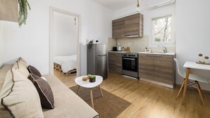 Une cuisine compacte équipée d’un réfrigérateur, d’un four et d’un évier, un petit coin repas avec une table et une chaise, et un canapé dans l’espace salon.