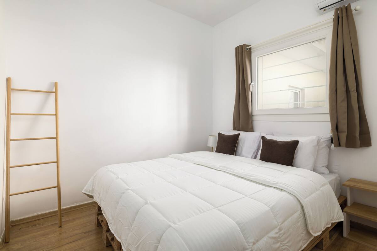 Un dormitorio con cama, una escalera de madera, una ventana con cortinas y una mesita de noche.