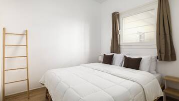 Een slaapkamer met een bed, een houten ladder, een raam met gordijnen en een nachtkastje.