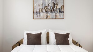 Un lit avec une literie blanche et deux oreillers, un tableau abstrait encadré au-dessus, et une tête de lit en bois.