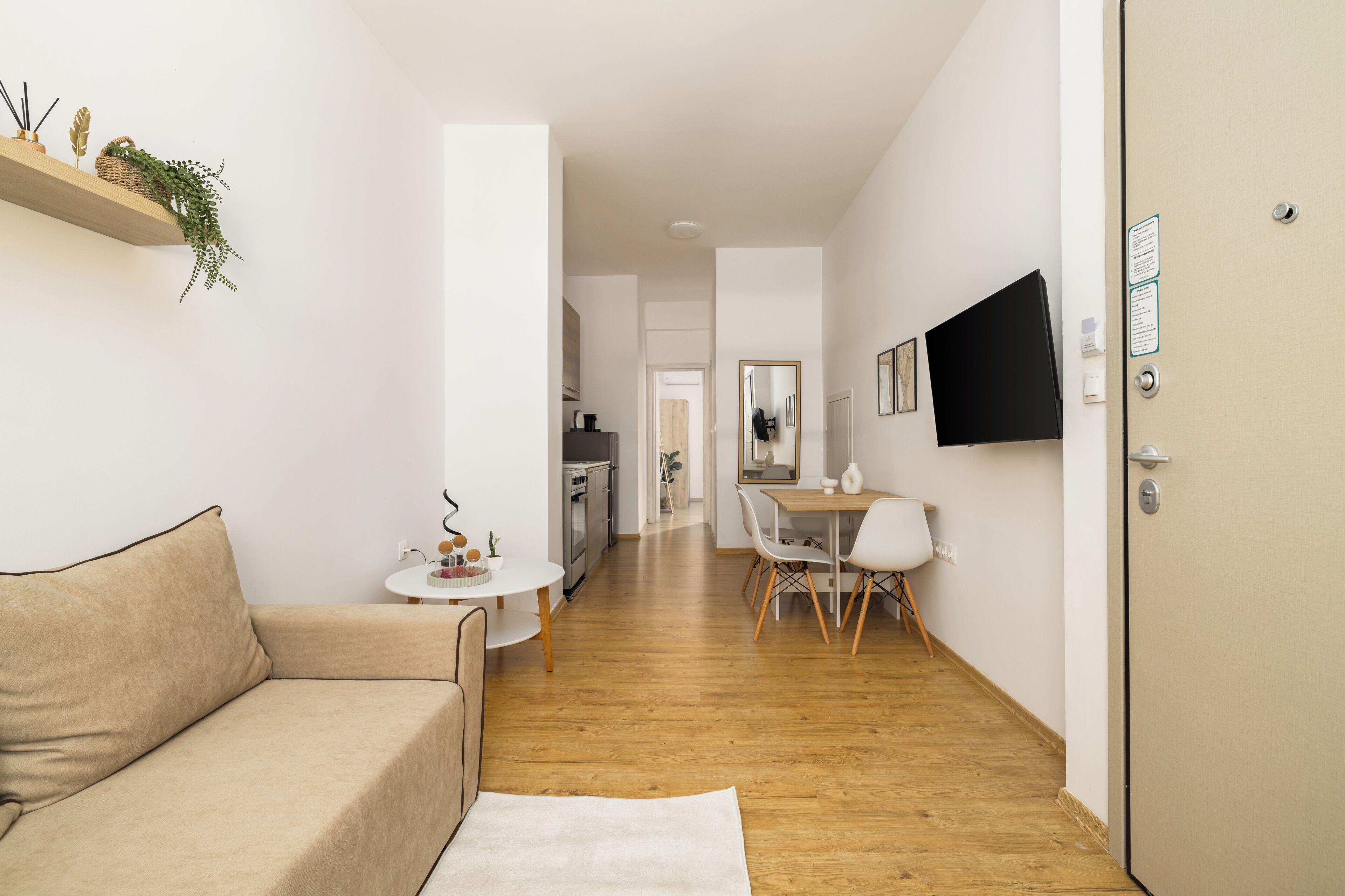 Ein modernes Wohnzimmer mit einer Couch, einem Esstisch mit Stühlen, einem an der Wand montierten Fernseher und Holzböden.