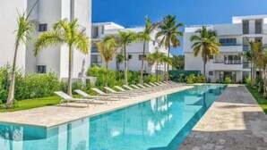 A swimming pool with lounge chairs, palm trees, and modern buildings in the background. - C5 -307 VISTA CANA / Panorama Lake (Punta Cana)