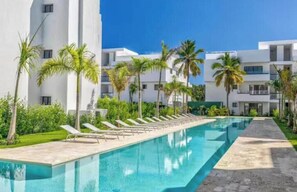 A swimming pool with lounge chairs, palm trees, and modern buildings in the background. - C5 -307 VISTA CANA / Panorama Lake (Punta Cana)