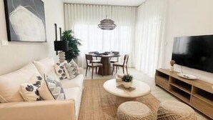 A modern living room with a sofa, coffee table, ottoman, TV, and dining area. - C5 -307 VISTA CANA / Panorama Lake (Punta Cana)