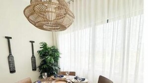 A dining area with a round wooden table, four chairs, a woven pendant light, a potted plant, and a wall-mounted decorative item. - C5 -307 VISTA CANA / Panorama Lake (Punta Cana)