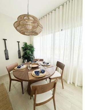 A dining area with a round wooden table, four chairs, a woven pendant light, a potted plant, and a wall-mounted decorative item. - C5 -307 VISTA CANA / Panorama Lake (Punta Cana)