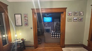 Una sala de estar con piso de madera, un televisor, fotos enmarcadas en la pared y un plaid a cuadros en el suelo.