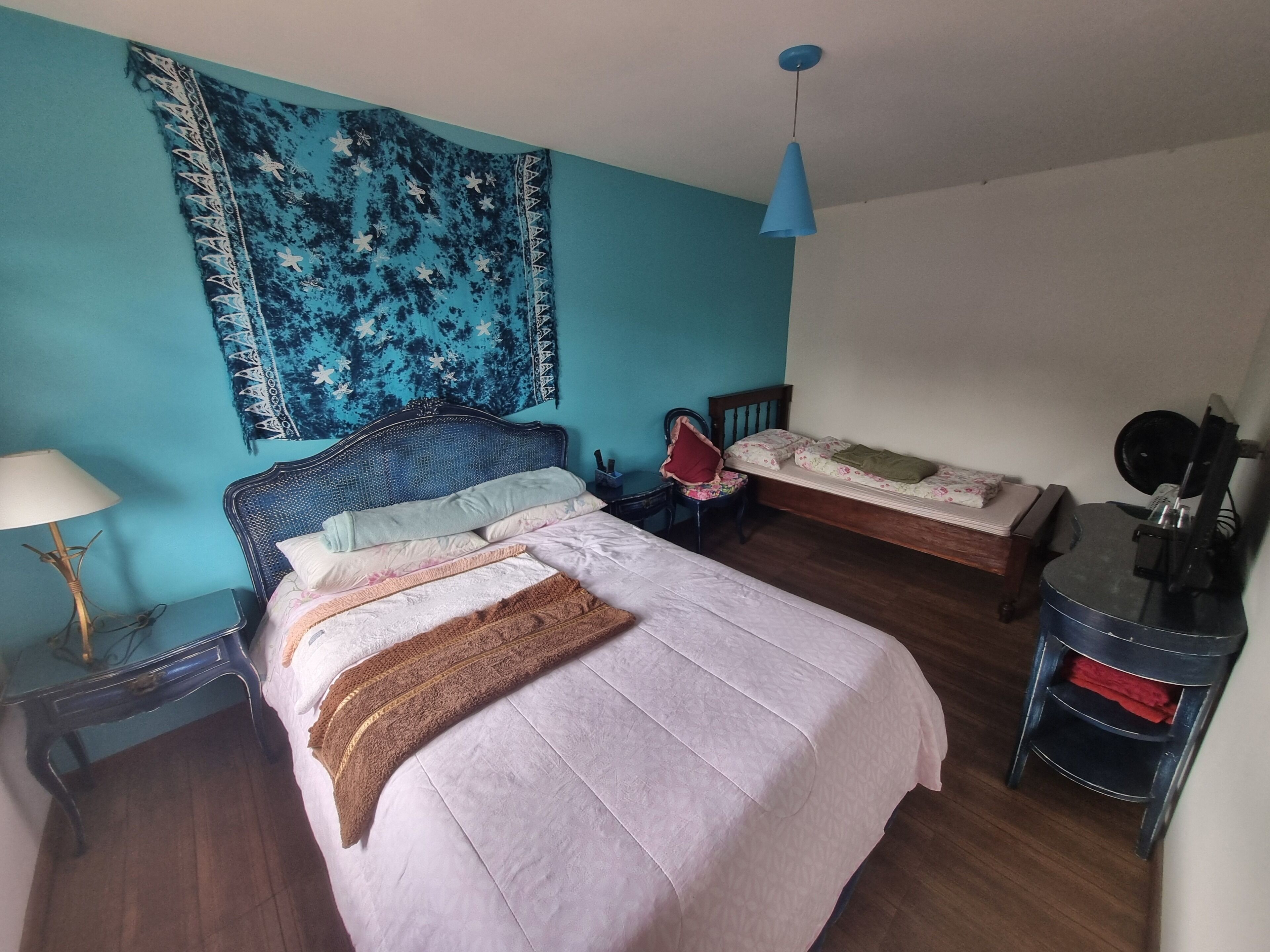 Een slaapkamer met een bed, een stoel, een nachtkastje, een lamp, een klein tafeltje en een wandtapijt.