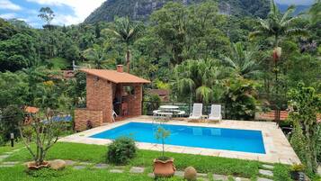Piscina com estrutura de tijolos, rodeada por vegetação exuberante e um cenário montanhoso.