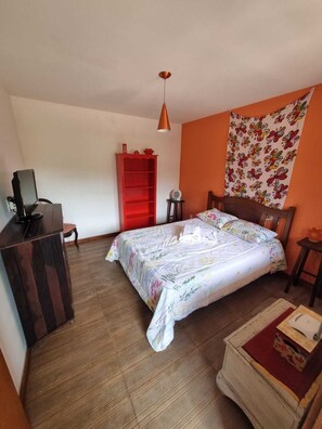 A bedroom with a bed, a desk with a computer, a red bookshelf, and a tapestry on the wall.
