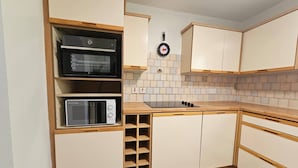 Una cocina compacta con electrodomésticos integrados, un microondas, una estufa y un reloj en la pared.