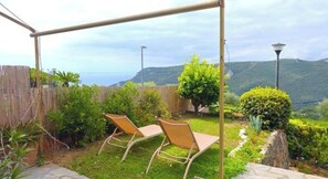 A patio with two chairs, a wooden fence, and a view of the sea. - Hostdomus - Plasch Apartment (Finale Ligure)