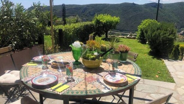 An outdoor dining area with a table set for two, surrounded by potted plants and a scenic mountain view. - Hostdomus - Plasch Apartment (Finale Ligure)