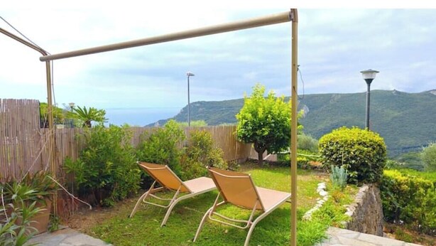 A patio with two chairs, a wooden fence, and a view of hills. - Hostdomus - Plasch Studio (Finale Ligure)