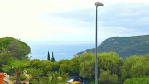A view of a lush green landscape with a clear sky, a tall street lamp, and a distant view of the sea. - Hostdomus - Plasch Studio (Finale Ligure)