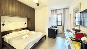 A hotel room with a bed, a desk, a chair, a ceiling fan, and a window. - Hostdomus - Plasch Studio (Finale Ligure)