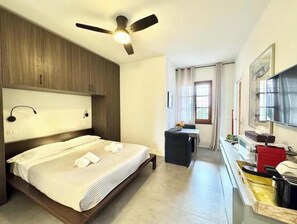 A hotel room with a bed, a desk, a chair, a ceiling fan, and a window. - Hostdomus - Plasch Studio (Finale Ligure)