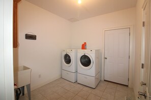 A laundry room with two stacked washing machines, a door, and a sign indicating the room's purpose. - Main House located on quiet cul-de-sac near town and walking trails to the water (Tisbury)