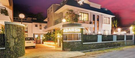 A modern two-story building with a gated entrance, a sign reading 'ADARSH,' and a parked car in front.