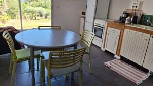 Cozinha com mesa e cadeiras, geladeira, forno e janela com vista para o verde.