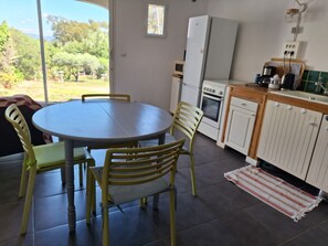 A kitchen with a dining table and chairs, a refrigerator, an oven, and a window with a view of greenery. - Loft 4 people 80 m² on the Presqu'île de Giens (Var) Vacation rental (Hyères)