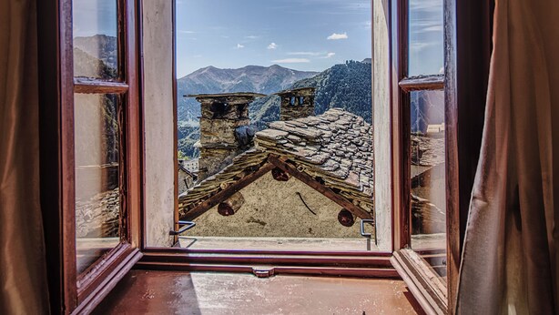 Een kamer met een raam dat uitkijkt op een bergachtig landschap.