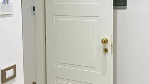 Una puerta blanca con picaporte de latón, un portero automático en la pared y un interruptor de luz.