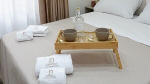 Habitación de hotel con cama, mesita de noche, bandeja con toallas y una botella, y una lámpara colgante.