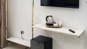 Habitación moderna con televisor montado, perchero de madera, estación de café y un pequeño electrodoméstico negro.