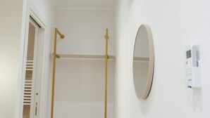 Un pasillo con un equipo de aire acondicionado blanco, un perchero de madera, un espejo y una puerta que da a un armario.