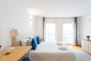 Ein Hotelzimmer mit Bett, Nachttischen, Schreibtisch, Lampe und Blick nach draußen.
