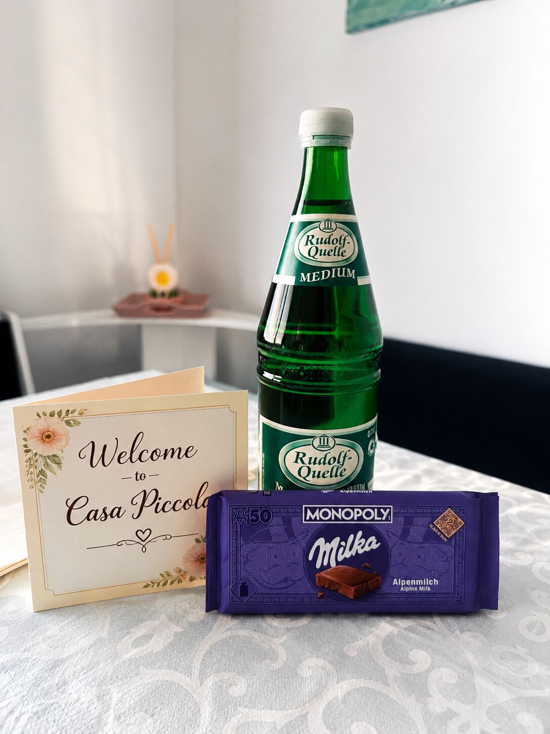 A bottle of Rudolf-Quelle medium, a welcome card, and a Monopolo Milka chocolate bar.