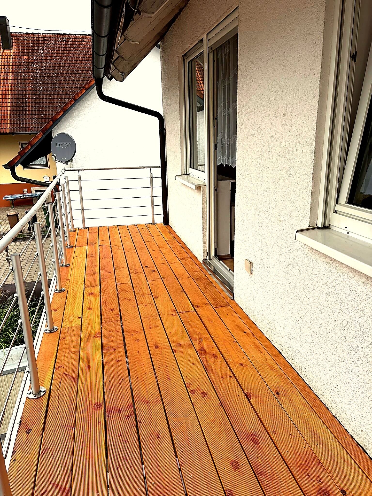 A wooden deck with a metal railing, a window with a white frame, and a building with a white exterior wall.