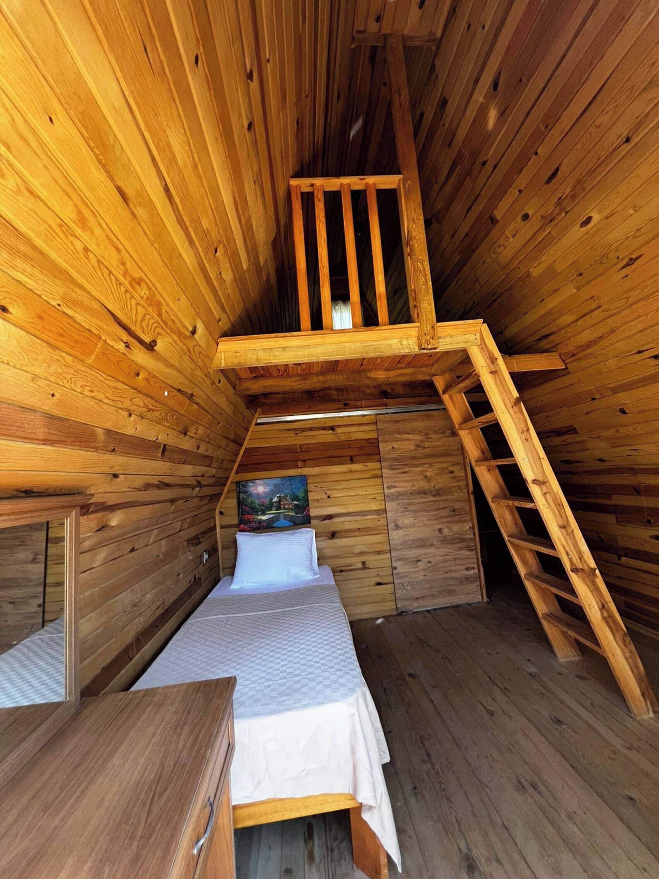 A wooden cabin with a loft bed, a ladder, and a painting on the wall.