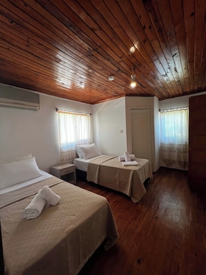 A room with two beds, wooden ceiling, white walls, and a door. - Don Kişot Pansiyon (Kumluca)