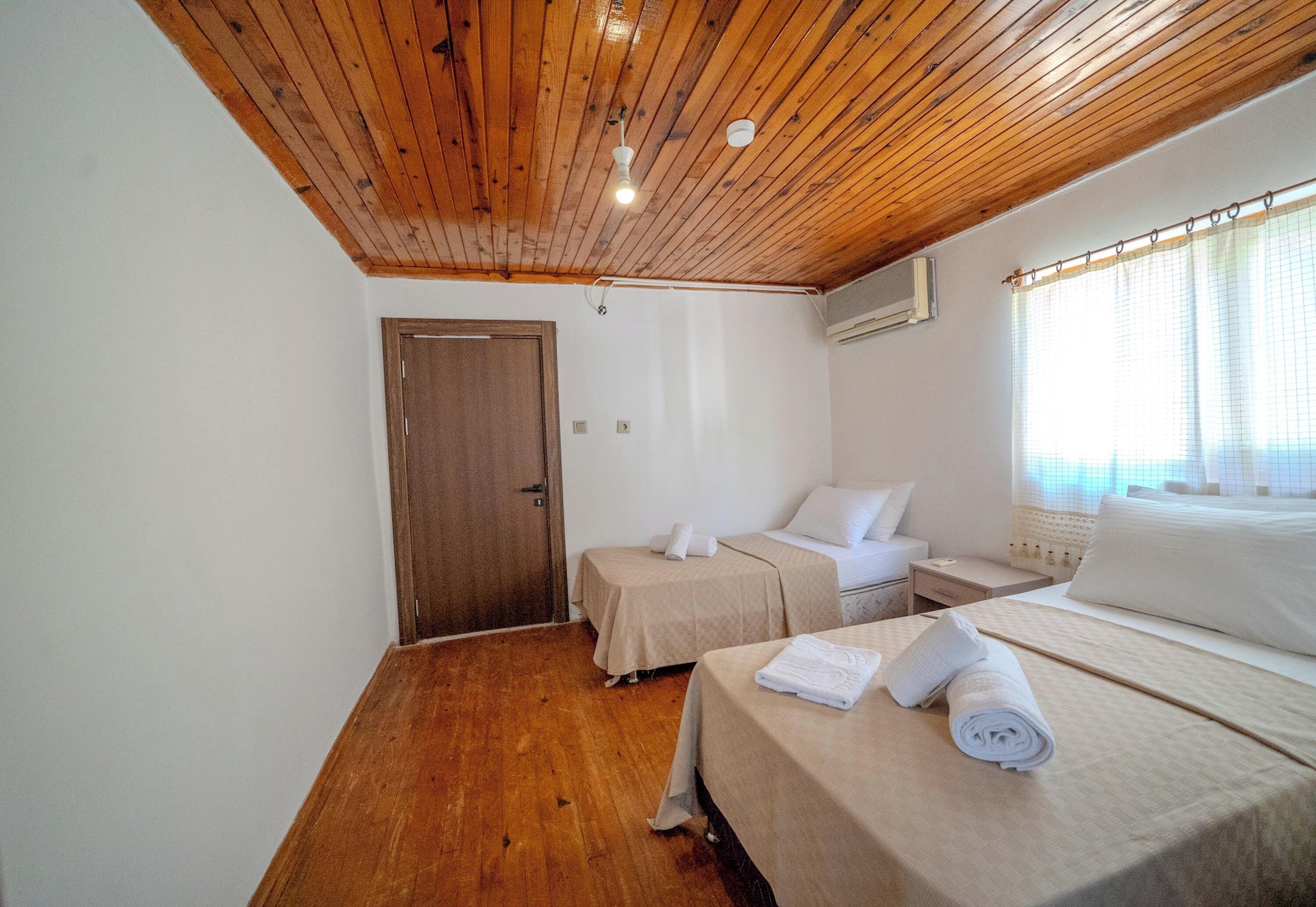 A bedroom with a wooden ceiling, two beds, a door, and a window with curtains.