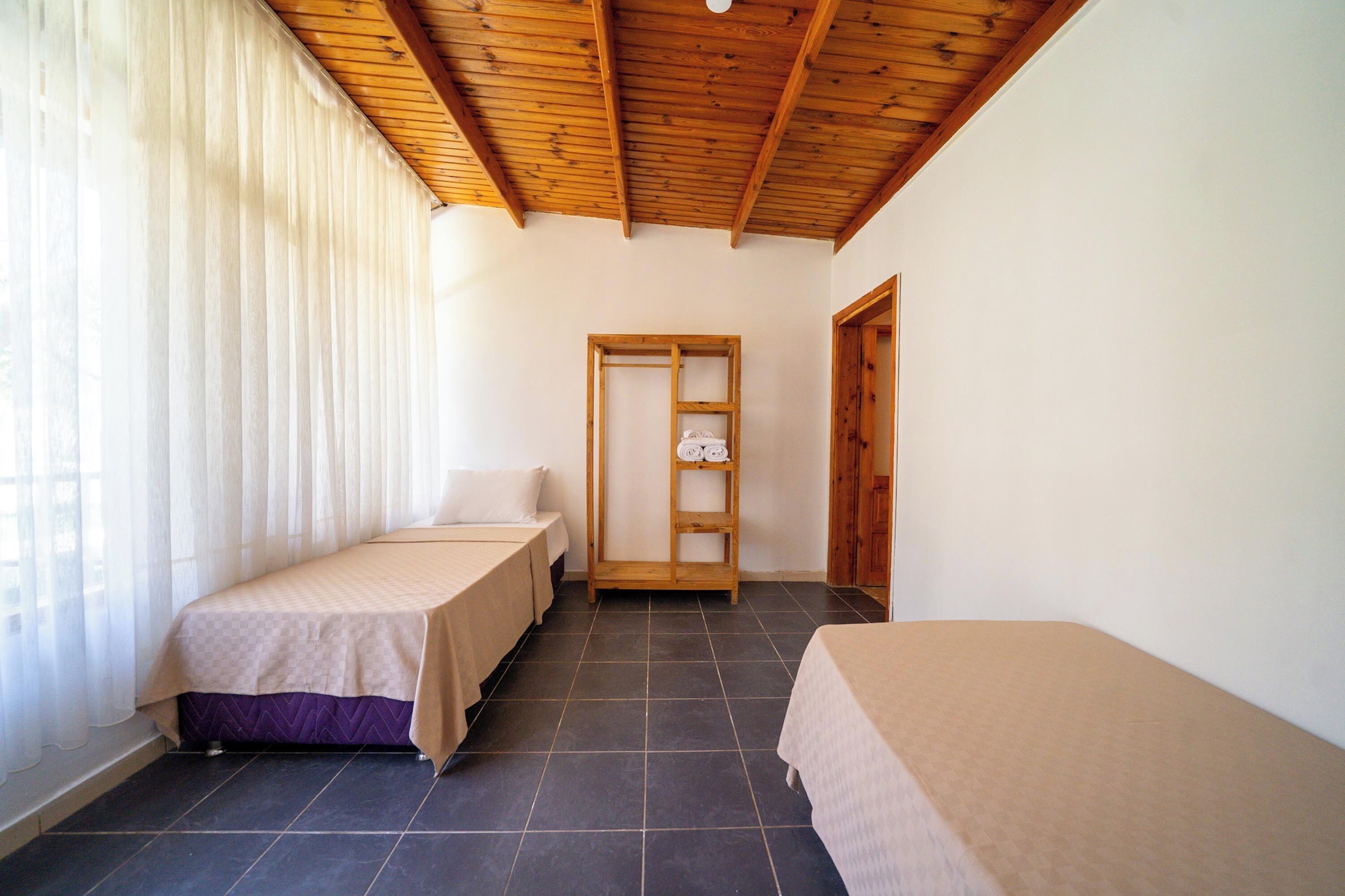 A room with two beds, a wooden ceiling, and a door leading to another room.