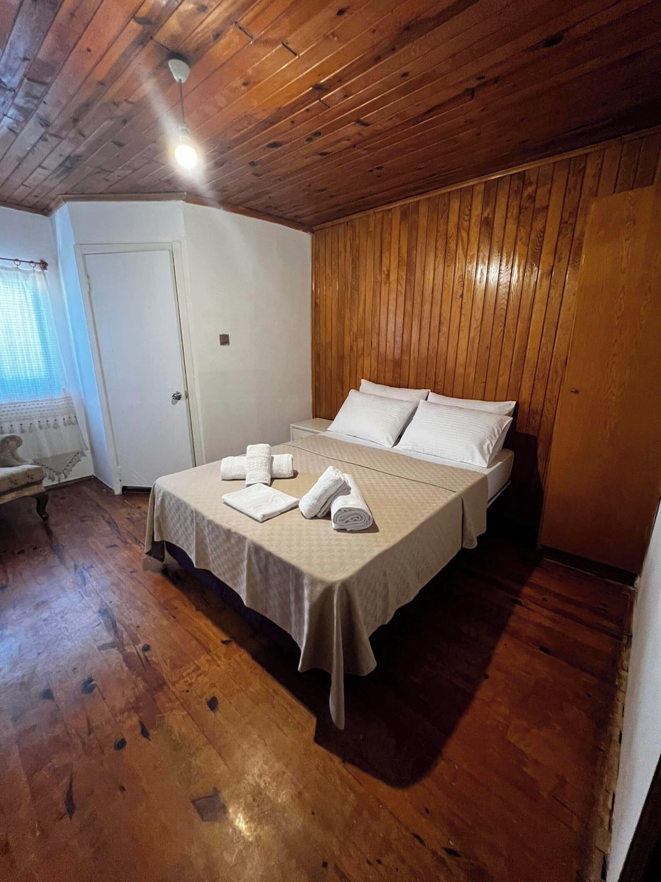 A bedroom with a wooden ceiling, a bed with white linens, and a bedside table with towels.