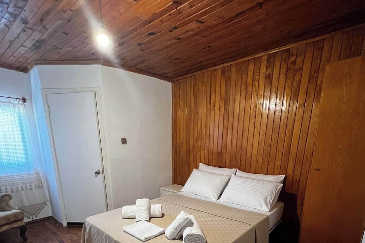A bedroom with a wooden ceiling, a bed with white linens, and a bedside table with towels.