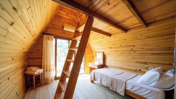 Un dormitorio de cabaña de madera con una cama en el altillo, una mesita con toallas y una ventana con cortinas.