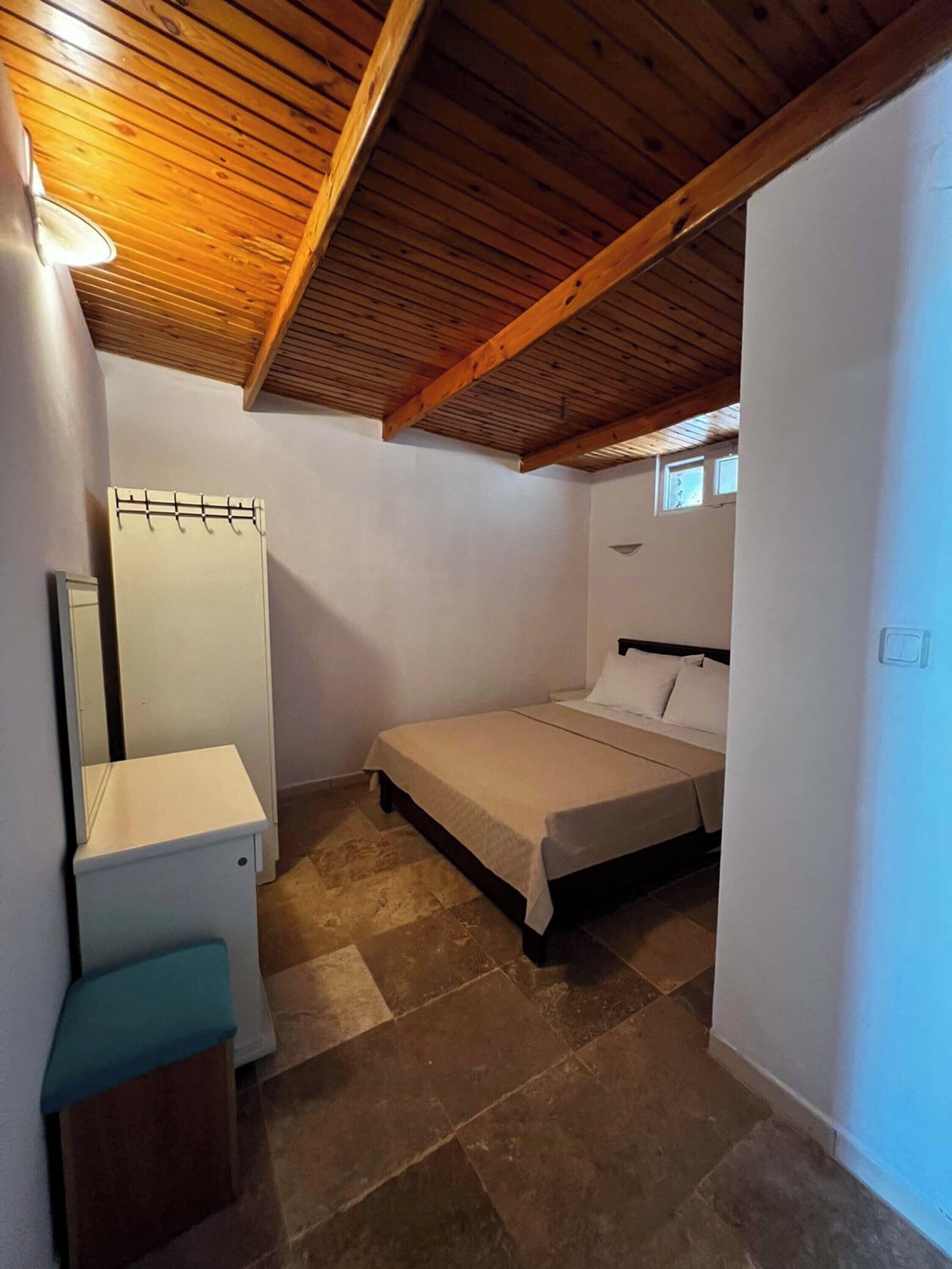 A small, single-room apartment with a sloped ceiling, a bed, a small desk, and a mirror.